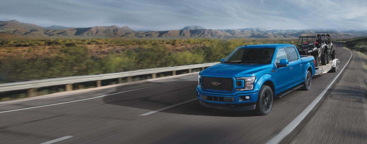 A blue 2019 Ford F-150 XLT is shown towing ATVs on a highway.