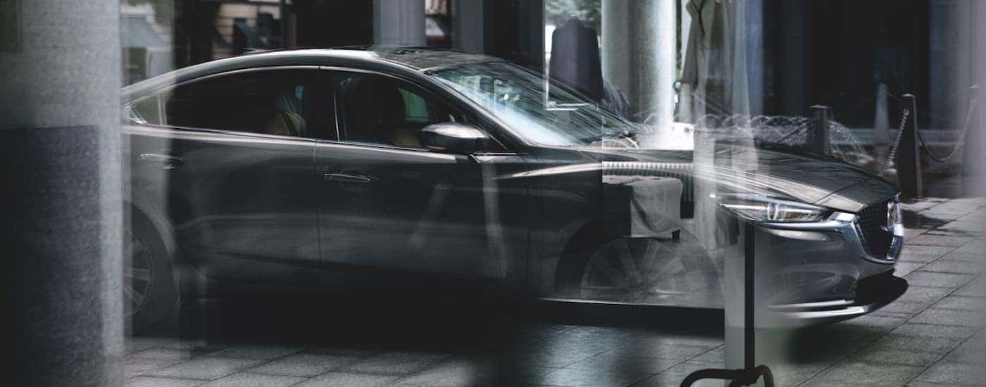 A grey 2021 Mazda6 is shown through glass in a city.