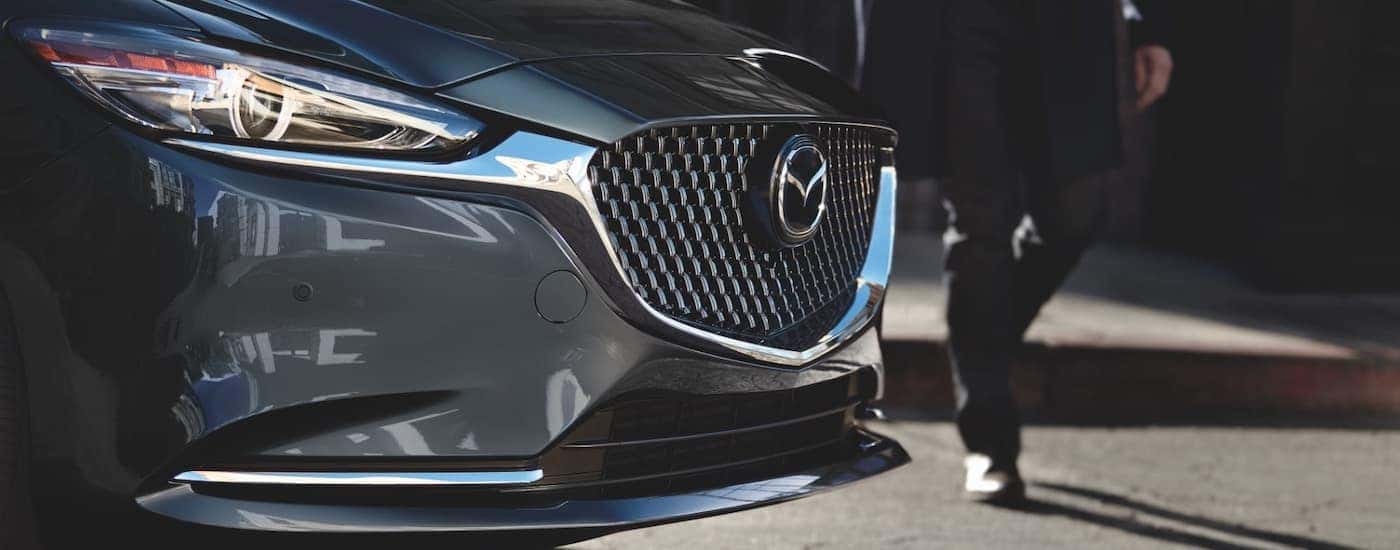 A person is shown walking past the grille of a grey 2021 Mazda6.