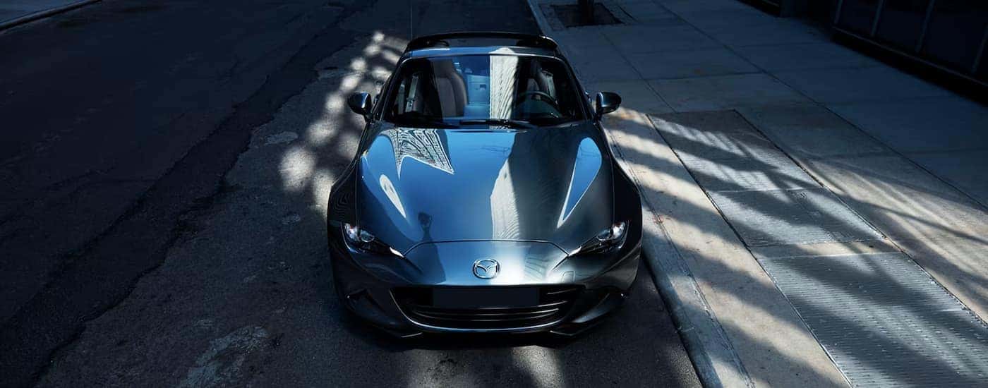 A blue 2023 Mazda Miata is shown from a high angle on a city street.