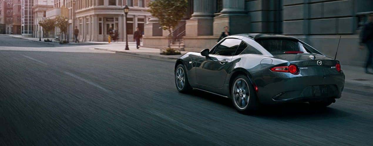 A dark grey 2023 Mazda MX-5 Miata RF is shown on a city street.