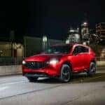 A red 2023 Mazda CX-5 is shown parked on a city street at night.