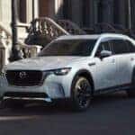 A white 2024 Mazda CX-90 for sale near Lexington, SC is shown on a city street.