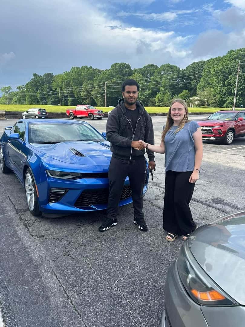 people shaking hands in front of camaro