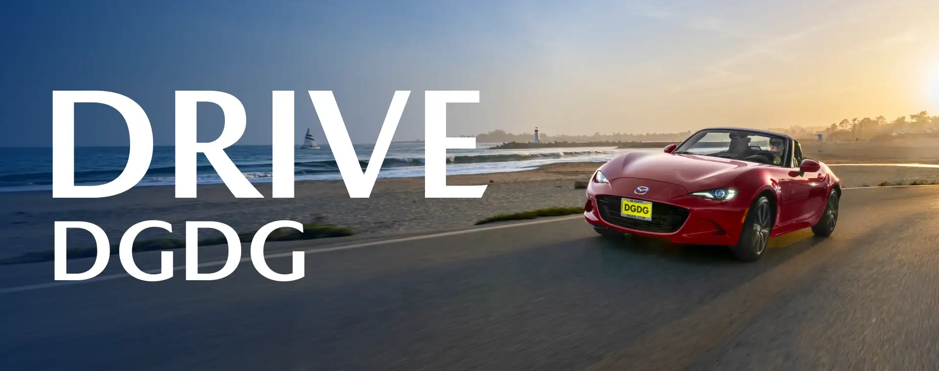 Red Mazda MX-5 Miata convertible driving along a coastal road next to a sandy beach at sunset.