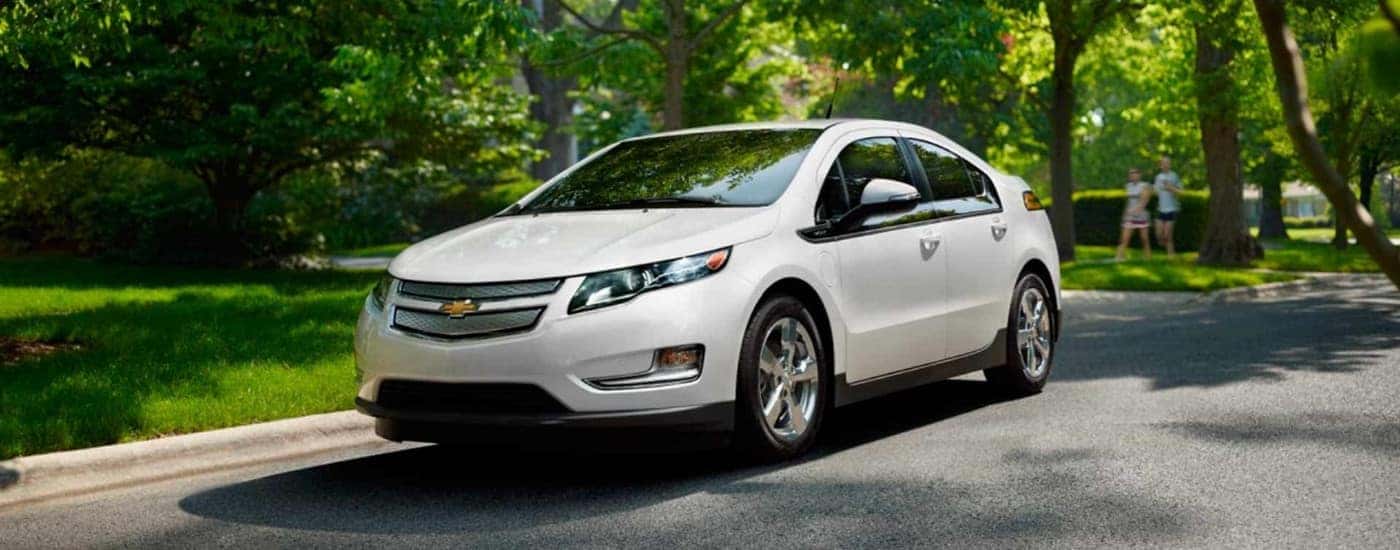 A white 2015 Chevy Volt is shown driving to a Chevy dealer.