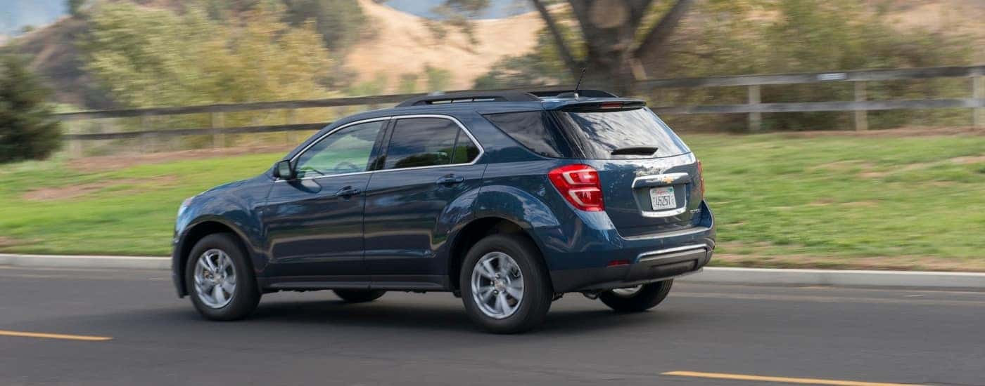 A blue 2016 Chevy Equinox for sale is shown driving past a fence.