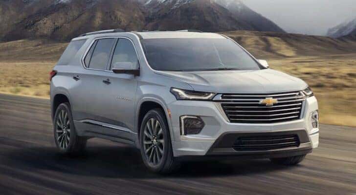 A silver 2022 Chevy Traverse is shown driving to a used car dealer.