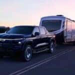A black 2025 Chevy Silverado EV RST is shown towing a trailer.