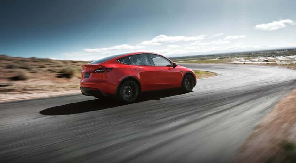 A red 2023 Tesla Model Y is shown driving to look at used EVs for sale.
