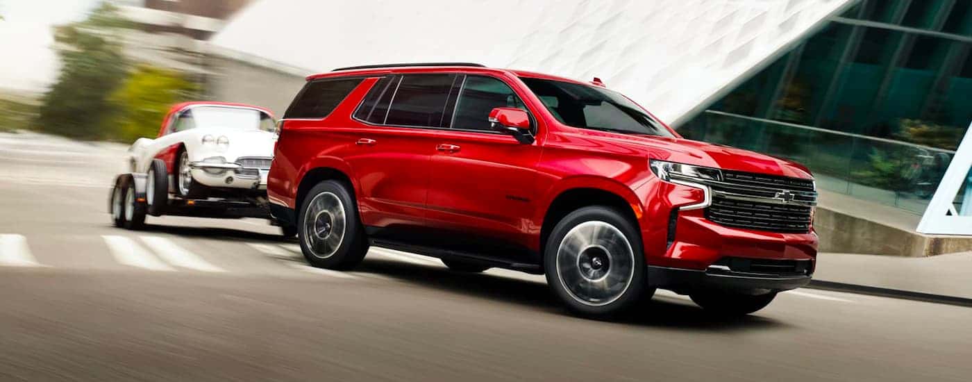 A red 2023 Chevy Tahoe towing a car around a bend.