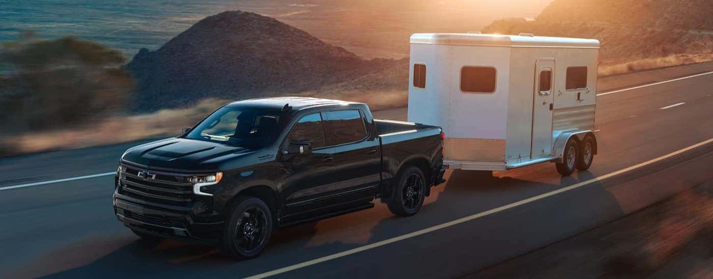 A black 2025 Chevy Silverado 1500 High Country towing a trailer.