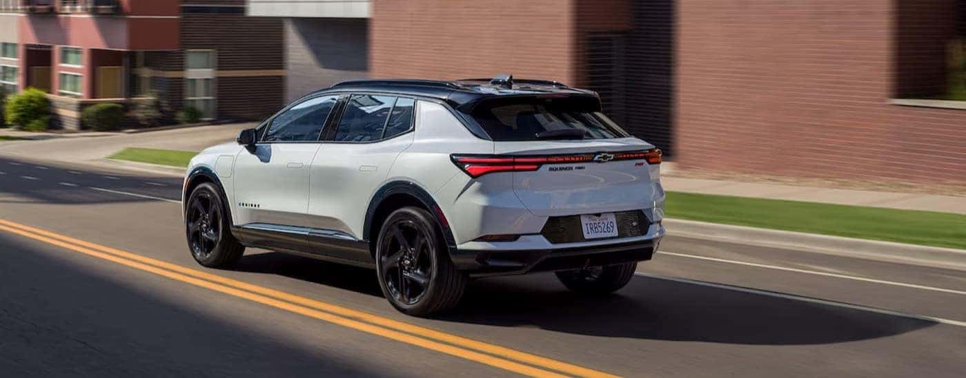 A white 2025 Chevy Equinox EV RS driving on a city street.