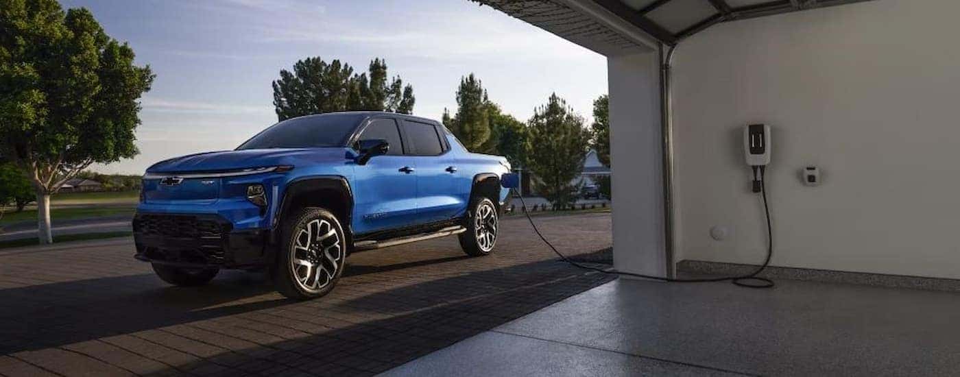 A blue 2025 Chevy Silverado EV charging outside a garage