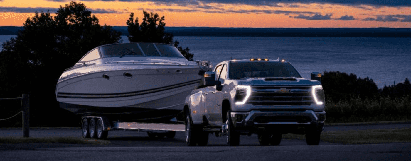 White 2025 Chevy Silverado 3500 towing a boat at night