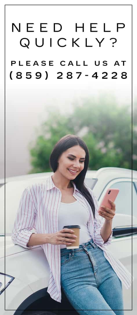 A woman leaning against the car texting. 