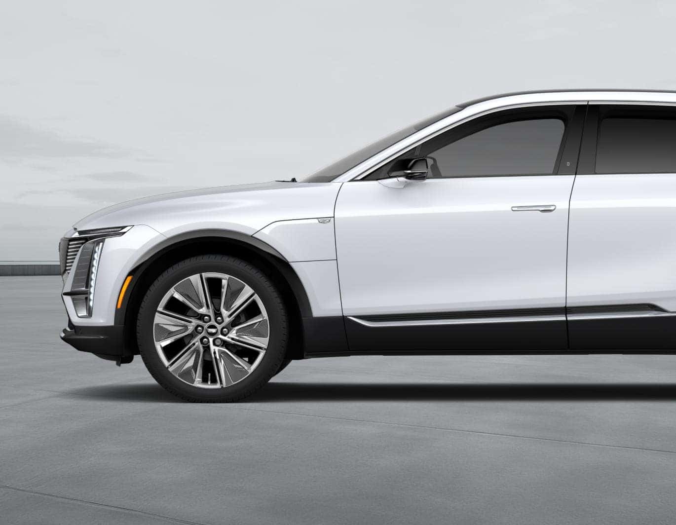 White Cadillac SUV shown in side profile highlighting its front wheel, vertical LED lighting, and chrome exterior accents.