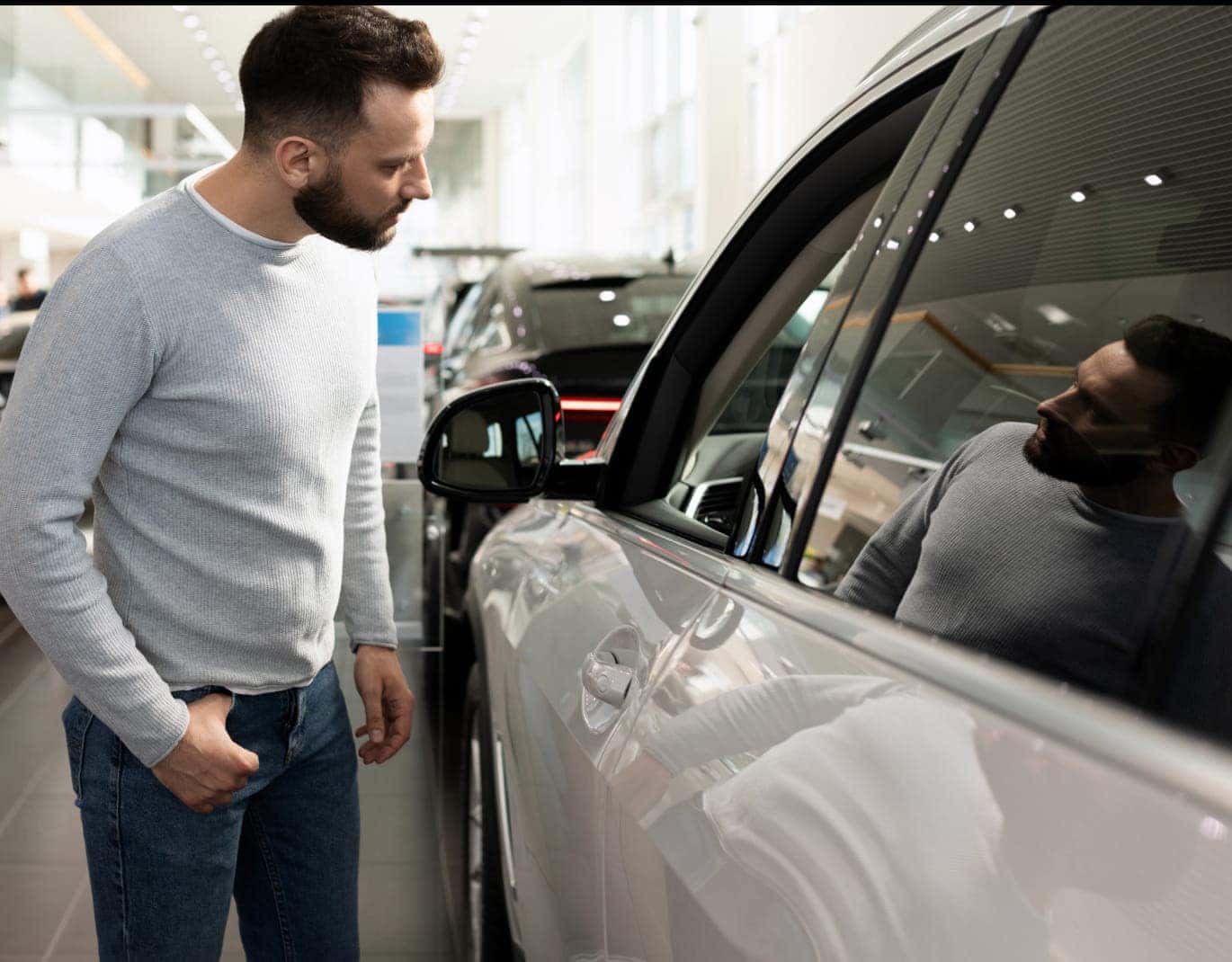 Man examining the exterior of a vehicle inside a dealership showroom.