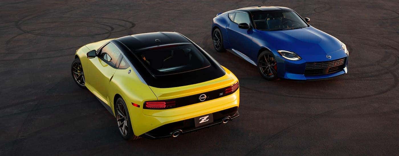 A yellow and a blue 2023 Nissan Z are shown parked facing in opposite directions on pavement with tire marks.
