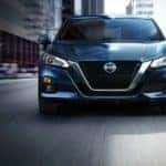 A blue 2021 Nissan Altima is shown driving from the front after leaving a Nissan service center.