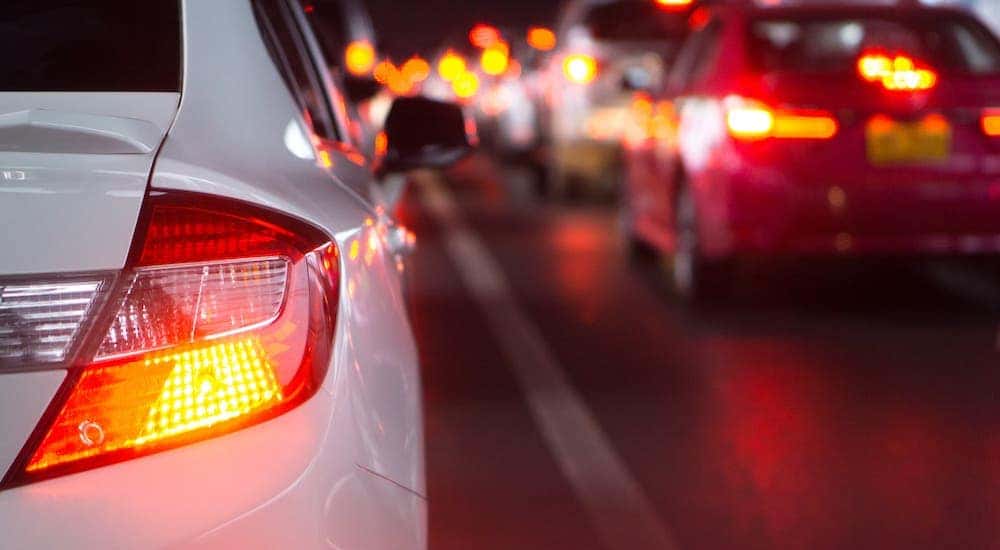 A closeup shows the brake light on a white sedan driving in the city at night.