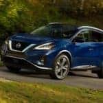 A blue 2021 Nissan Murano is driving in front of trees as part of a Nissan end of lease test drive.