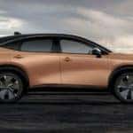 A bronze 2022 Nissan Ariya is shown from the side under a cloudy sky.