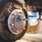 A close up shows a Nissan brake service being done by a gloved mechanic.