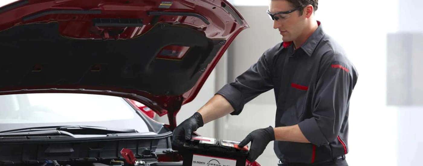 A Nissan technician is replacing the battery on a red vehicle.