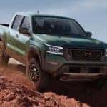 A green 2022 Nissan Frontier is shown from the front off-roading through the desert.