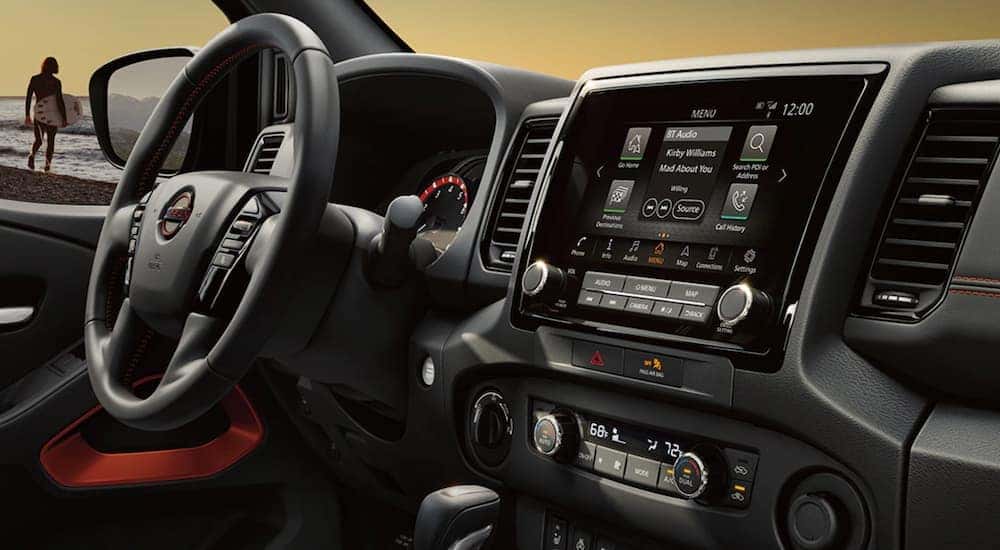 The black interior of a 2022 Nissan Frontier shows the steering wheel and infotainment screen.