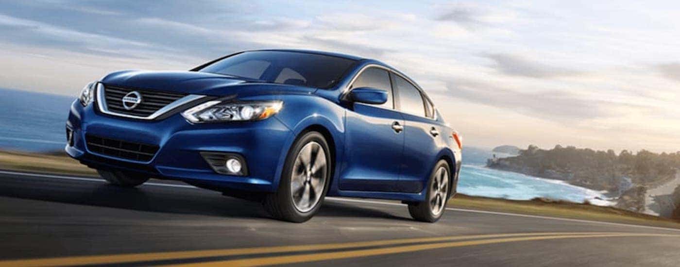 A blue 2018 certified pre-owned Nissan Altima is shown driving near a body of water.