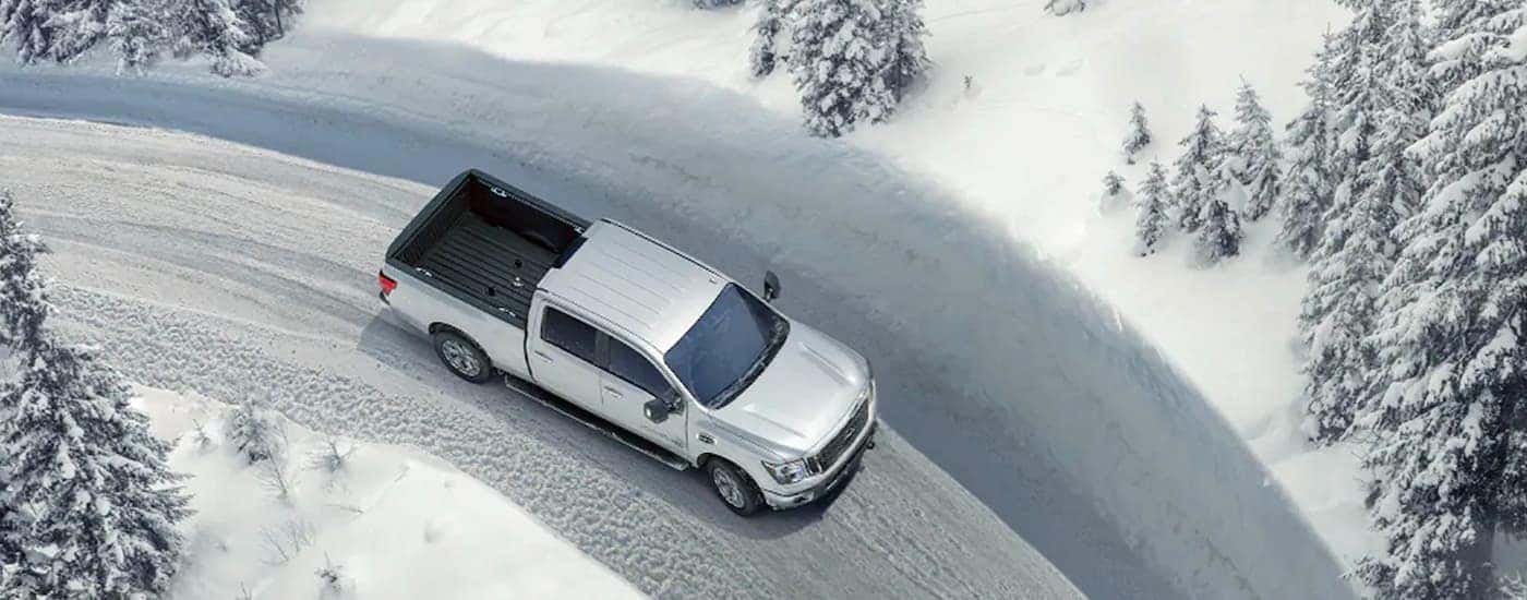 A silver 2021 Nissan Titan is shown from a high angle driving on a plowed road.
