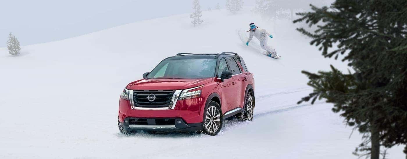 A red 2022 Nissan Pathfinder is shown parked on a snowy mountain next to a snowboarder.