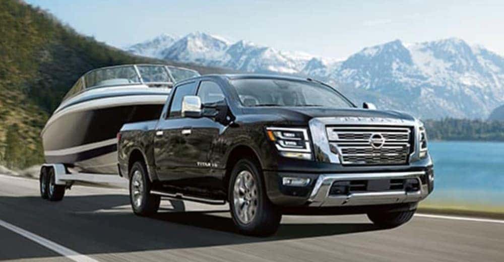 A black 2020 Nissan Titan is shown towing a boat near a body of water.