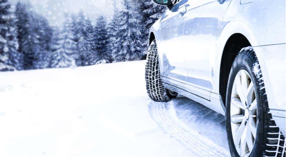 A car is shown driving through snow after looking for snow tires for sale.