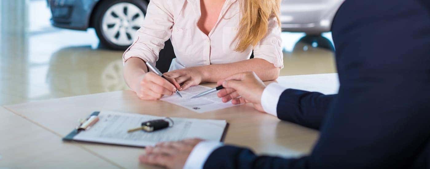 A person is shown filling out finance papers at a Tinley Park Nissan dealer.