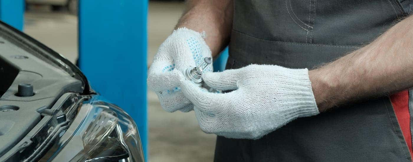 A close up shows a technician changing a headlight bulb.