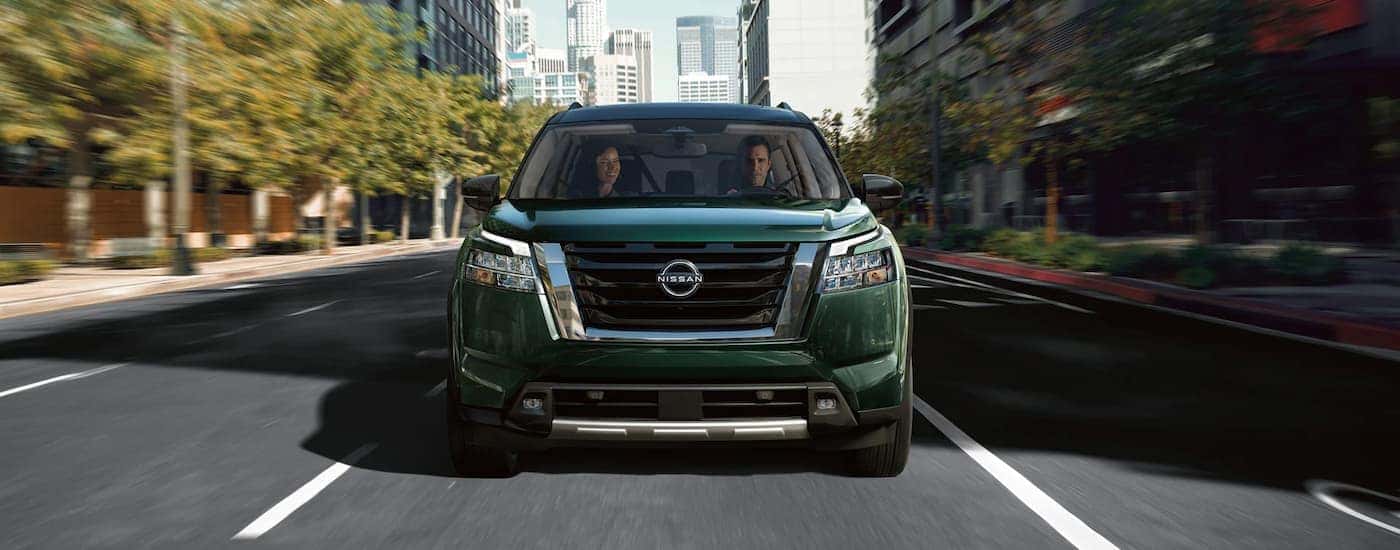 A dark green 2022 Nissan Pathfinder is shown from the front driving on a city street.