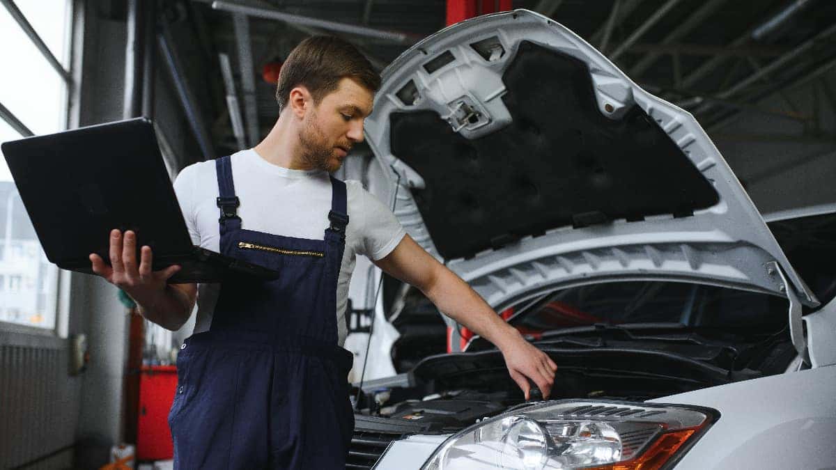 A man performing vehicle maintenance on a white car with the hood open.