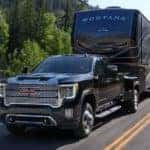 A black 2022 GMC Sierra 3500HD Denali is shown towing a trailer past a river.