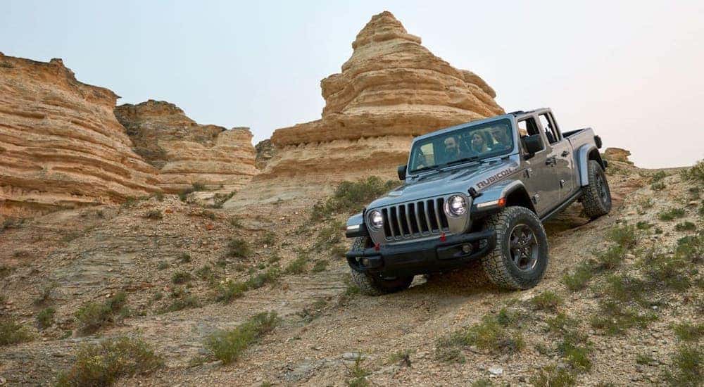 A silver 2020 Jeep Gladiator is descending a rock trail with the roof off.