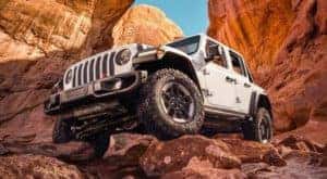 A white Jeep Wrangler Unlimited is parked on a rock formation.