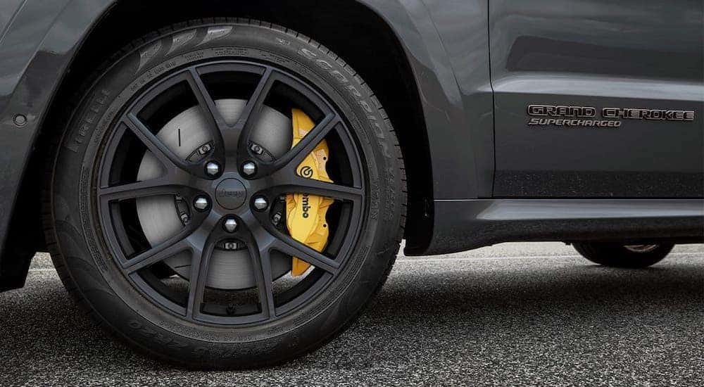 A closeup is shown of the wheel with yellow Brembo brakes and Supercharged badging on a dark gray 2020 Jeep Grand Cherokee Trackhawk.