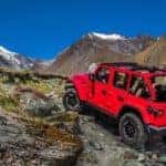 A red 2020 Jeep Wrangler Unlimited with no roof is climbing rocks up a mountain.
