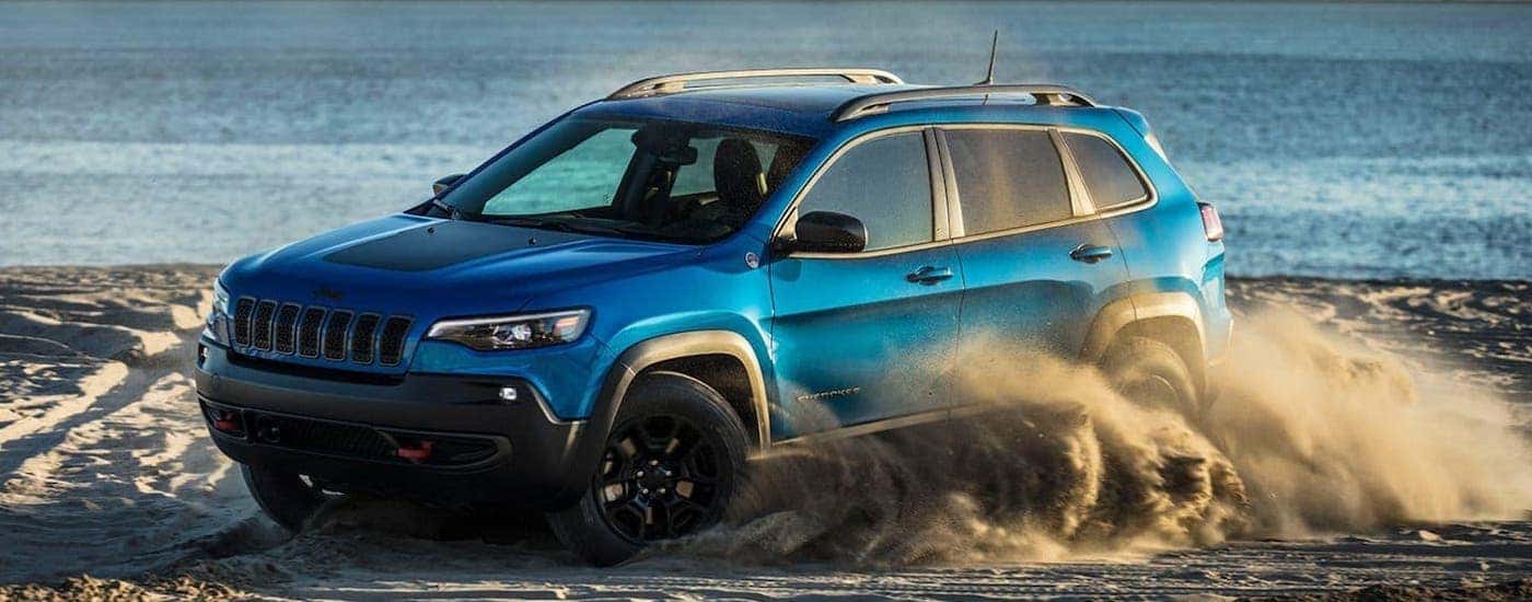 A blue 2020 Jeep Cherokee is kicking up sand on a beach.