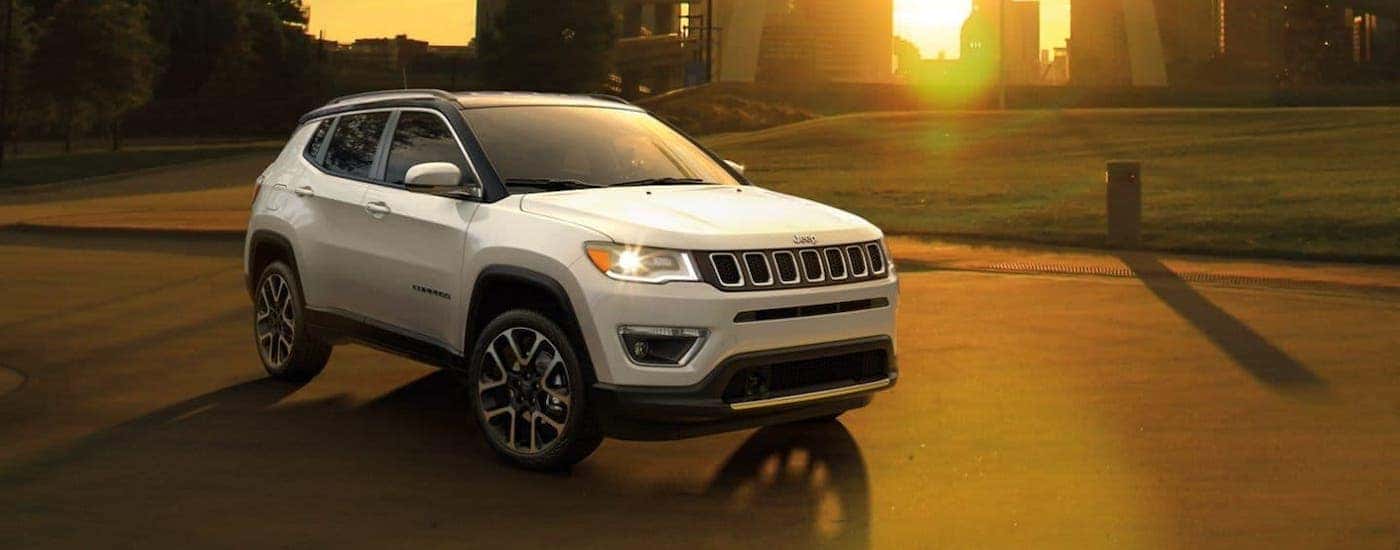 A white 2020 Jeep Compass is parked in front of a city skyline at sunset.