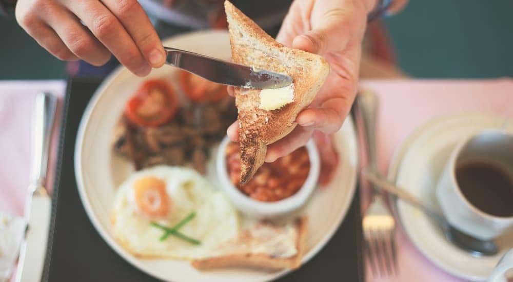 An above angle shows a man putting butter on toast above a plate of breakfast food.