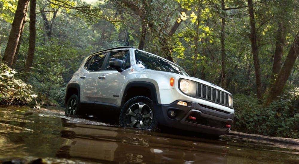 A silver 2020 Jeep Renegade Trailhawk is shown crossing a river on a woodland trail.
