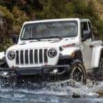 A white 2021 Jeep Wrangler, one of the new Jeeps for sale, is crossing a river while off-roading.